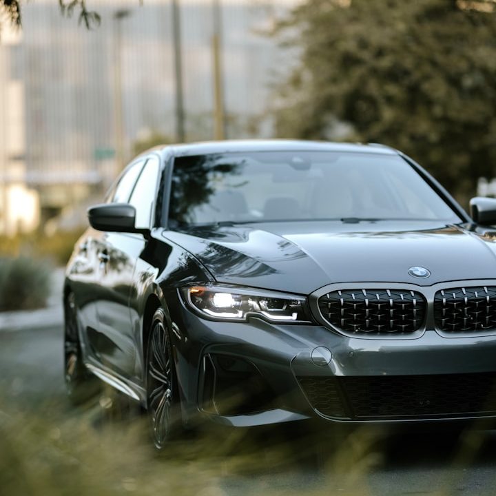 Kfz-Gutachten Ein schwarzer BMW fährt auf einer grünen, bewaldeten Straße.